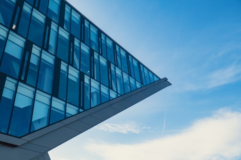 Moderno edificio de oficinas exterior con fachada de vidrio sobre fondo claro del cielo.