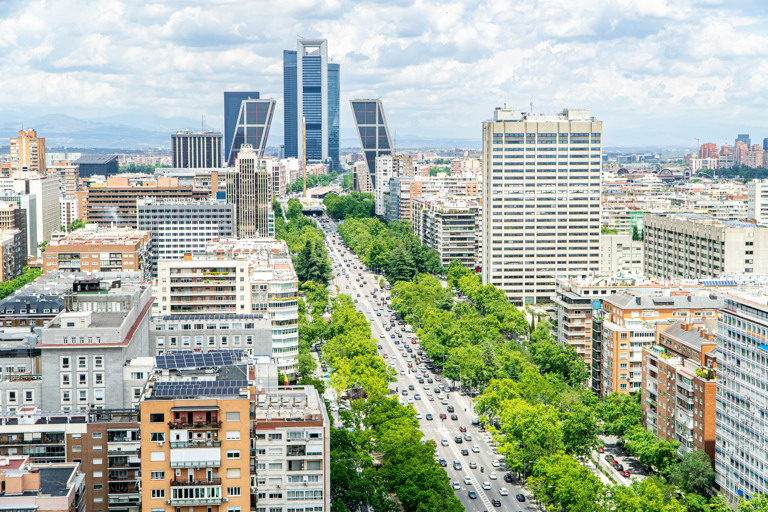Vista panorámica de Madrid con rascacielos modernos y edificios residenciales que rodean una amplia avenida con tráfico.