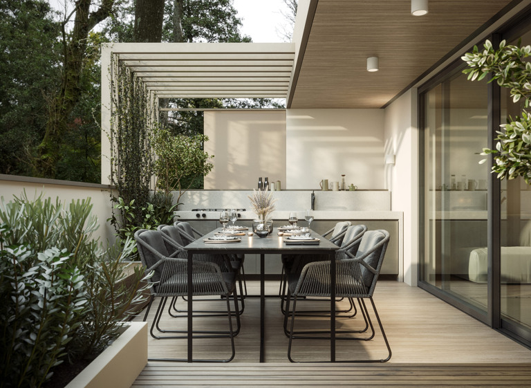 Terraza moderna decorada con un estilo minimalista, que incluye una mesa de comedor con sillas acolchadas, una pérgola con plantas trepadoras y una cocina al aire libre. La terraza está rodeada de vegetación y cuenta con una elegante iluminación y acabados en tonos neutros.